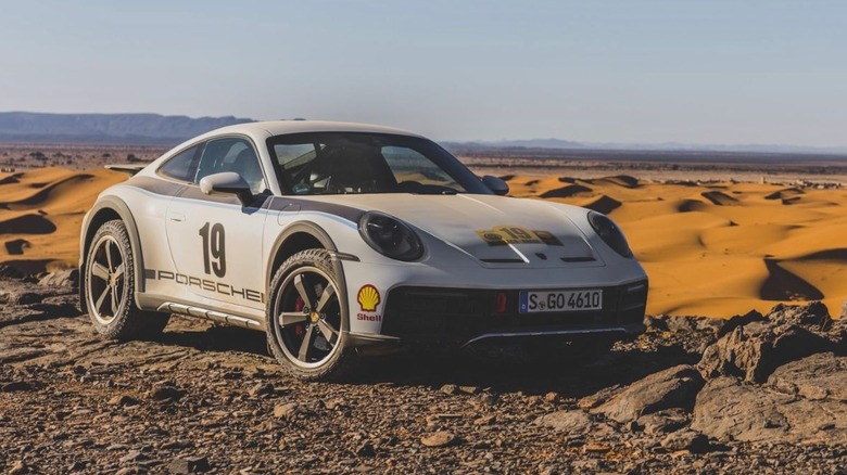 Front 3/4 view of Porsche 911 Dakar parked near desert dunes.