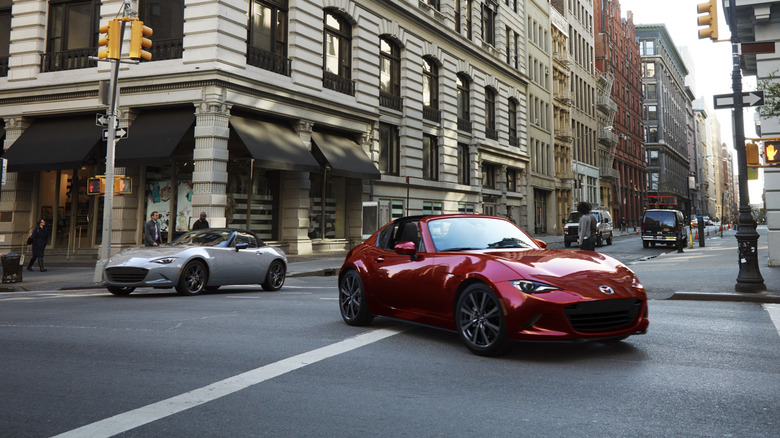 Two Mazda Miatas on a city street, one red and one gray