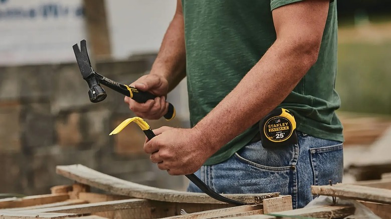 A person using the Stanley Wonder Bar Pry Bar and a hammer on lengths of wood