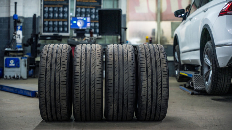 A set of summer tires stacked next to each other near a car in a workshop.