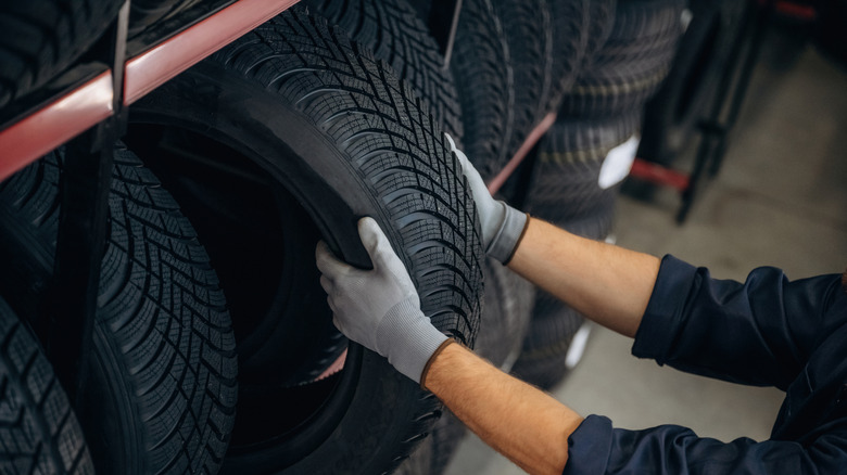 A person wearing gloves taking a brand-new tire from a rack with other tires.