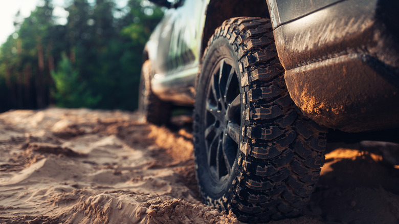 Close up of a rugged SUV with all-terrain tires on sandy ground.