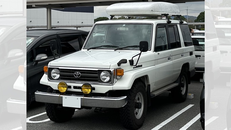 a white five-door Toyota Land Cruiser J70 with a white top box in a parking lot
