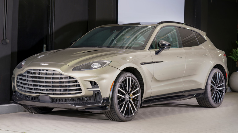 A sand gray metallic Aston Martin DBX 707 parked in front of a building.