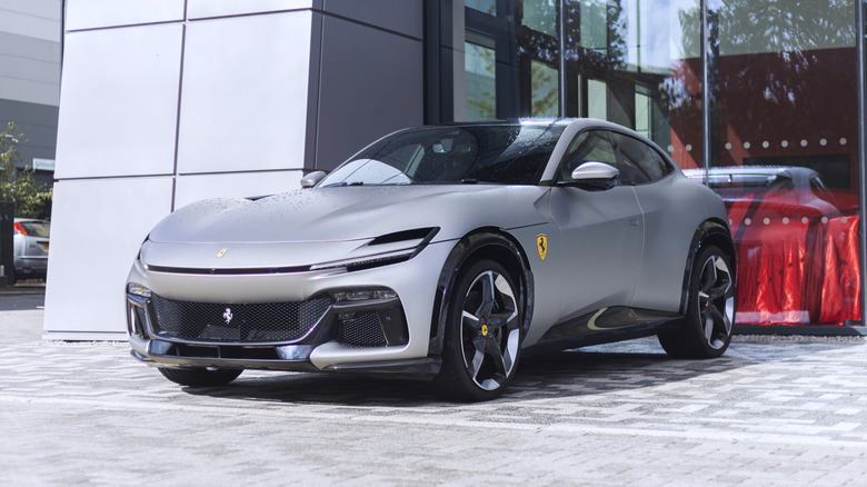 A silver Ferrari Purosangue SUV parked in front of a dealership.
