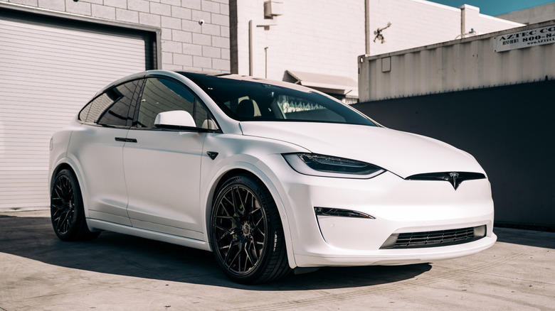A white Tesla Model X Plaid parked in front of an industrial building.