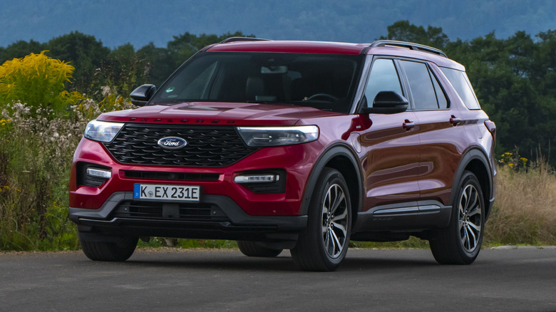 A red 2020 Ford Explorer hybrid being driven in a green country setting.