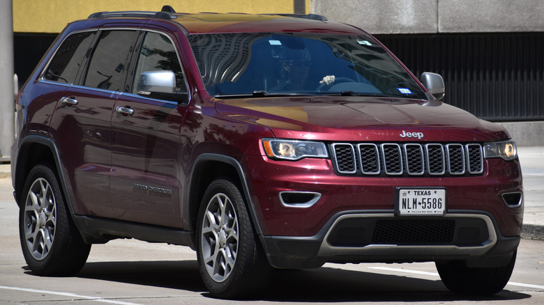 A front-end view of a red Jeep Grand Cherokee driving down a road.