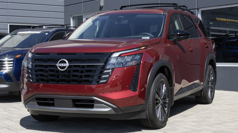 A red Nissan Pathfinder parked in front of a Nissan dealership.