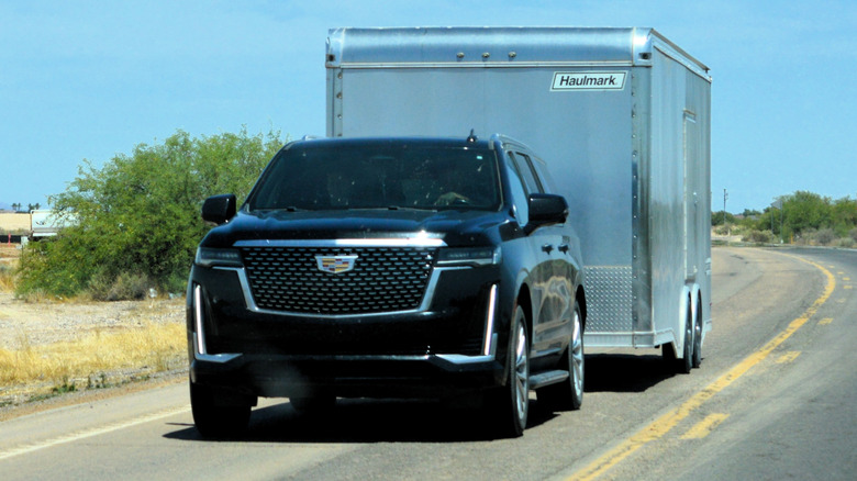 A black Cadillac Escalade SUV towing a large enclosed cargo trailer