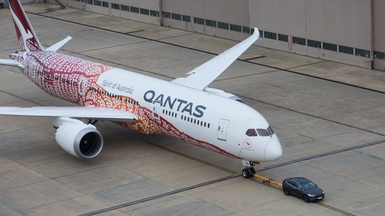 A Tesla Model X electric SUV towing a Qantas Boeing 787-9 Dreamliner on the tarmac
