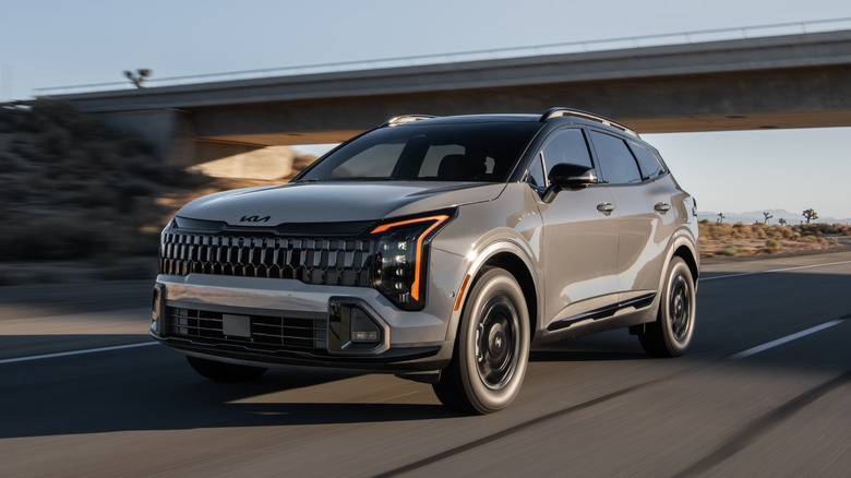 Light tan Kia Sportage driving on a road under an overpass