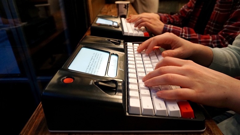 Two people sitting side by side using Freewrite smart typewriters in a cafe