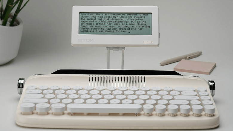 A white BYOK device on a stand behind a white mechanical keyboard