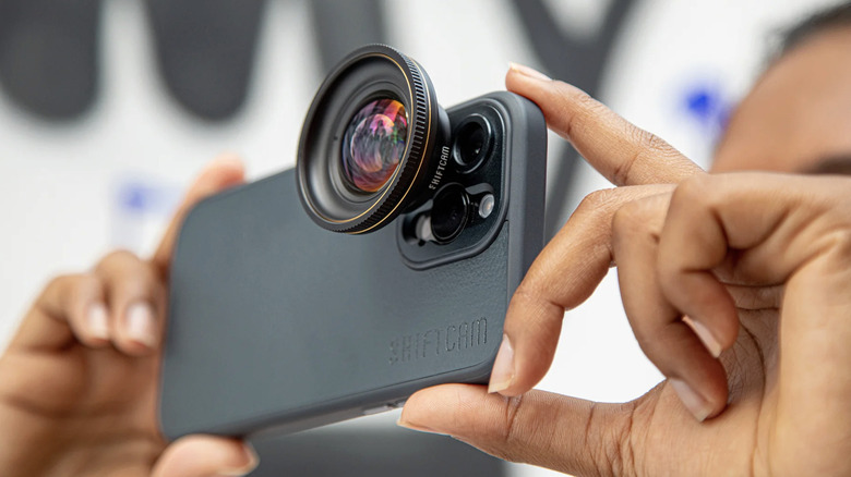A man holding iPhone with attached lens to its camera