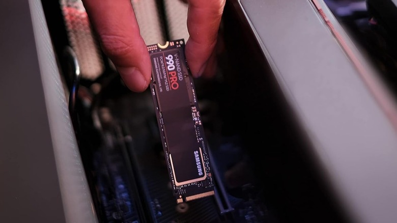 A Samsung 990 Pro SSD being held next to a computer's motherboard