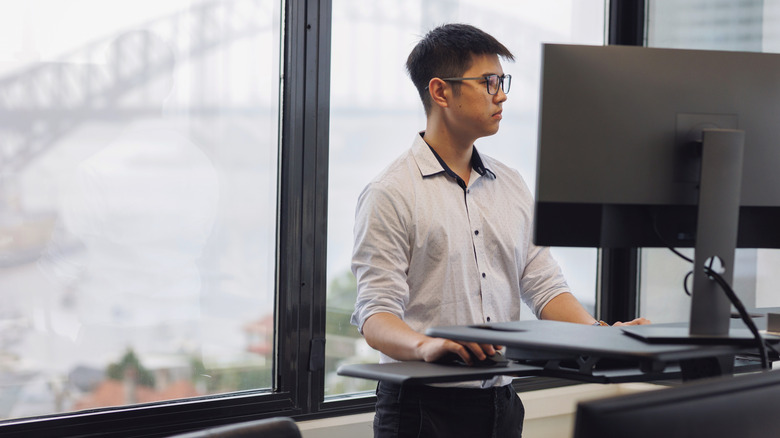 A young man working at a standing desk, cityscape window background