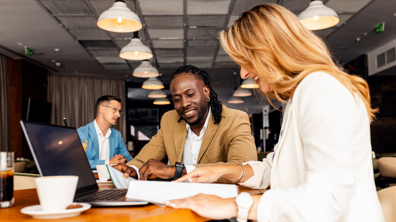 coworkers talking about work while using laptop in modern coffee shop