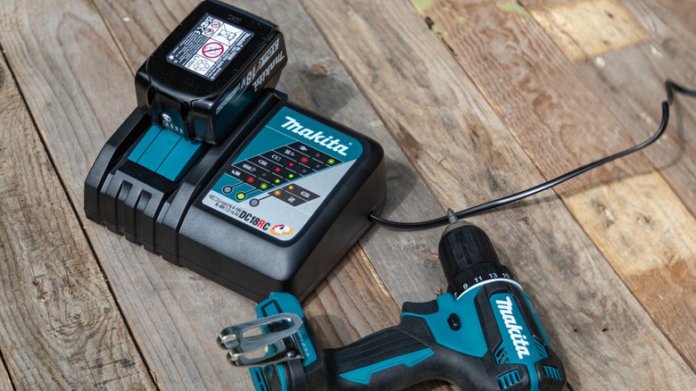 Charging Makita cordless drill battery alongside a Makita drill on a wooden surface.