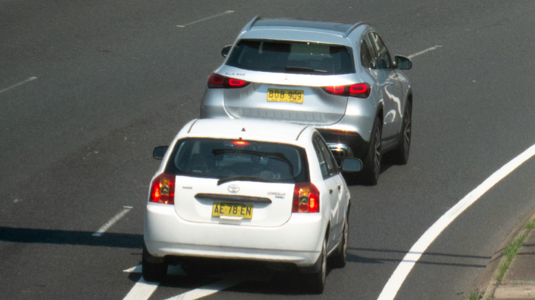 Two vehicles with New South Wales plates traveling down a road, with the car at the back tailgating the one in front.