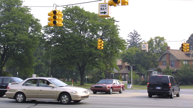Drivers proceed through a four-way intersection as traffic lights sit dark, hanging from an overhead wire.