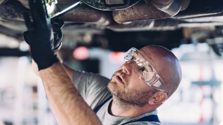 A mechanic wearing safety glasses while working underneath a car.