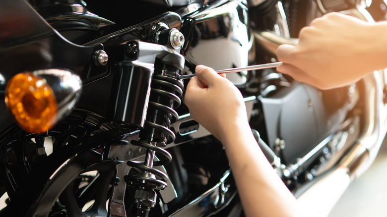 A mechanic using tools to repair and adjust the suspension on a motorcycle, with the background blurred.