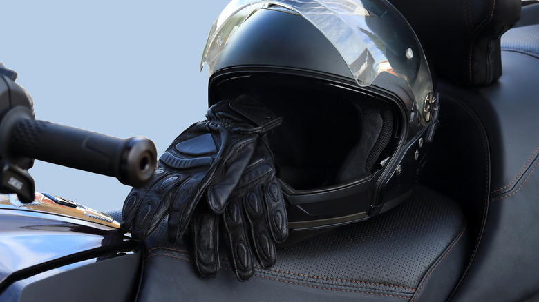 A motorcycle helmet and motorcycle gloves left resting on the seat of an unknown model bike in the sun.