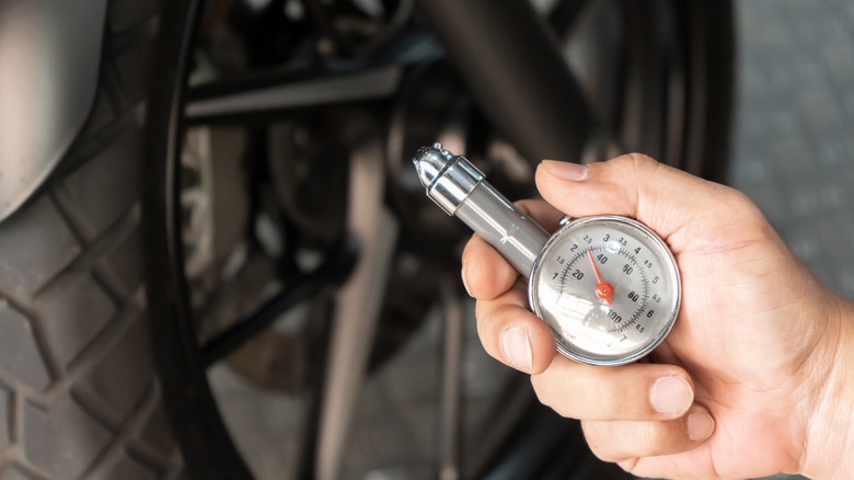 A man holding a silver tire pressure gauge for checking the PSI in a motorcycle tire, with only the gauge in focus.