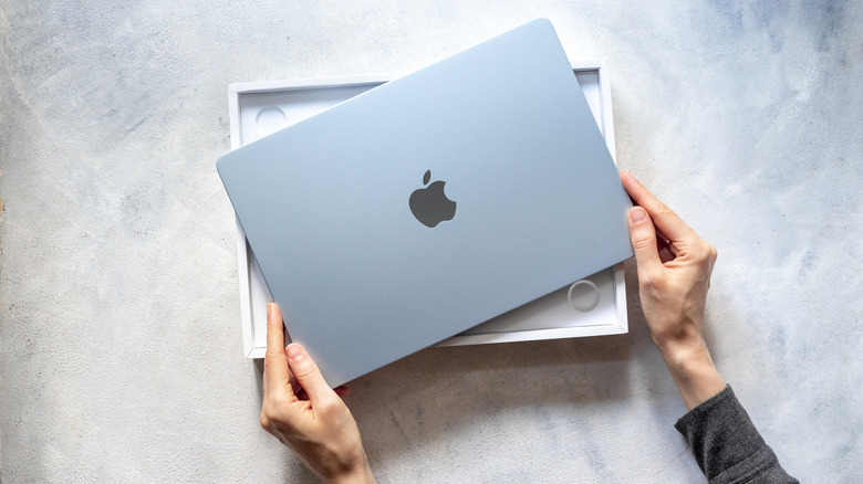 A person removing a MacBook from the box, top-down view