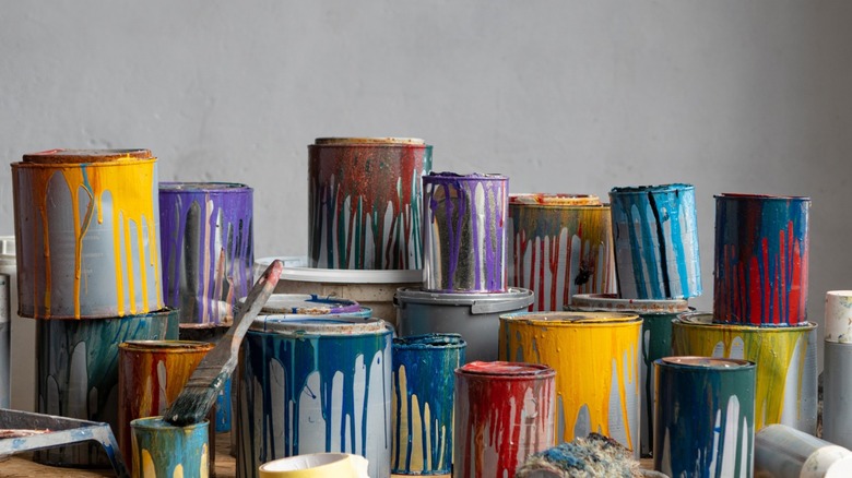 old paint cans piled against a gray wall.