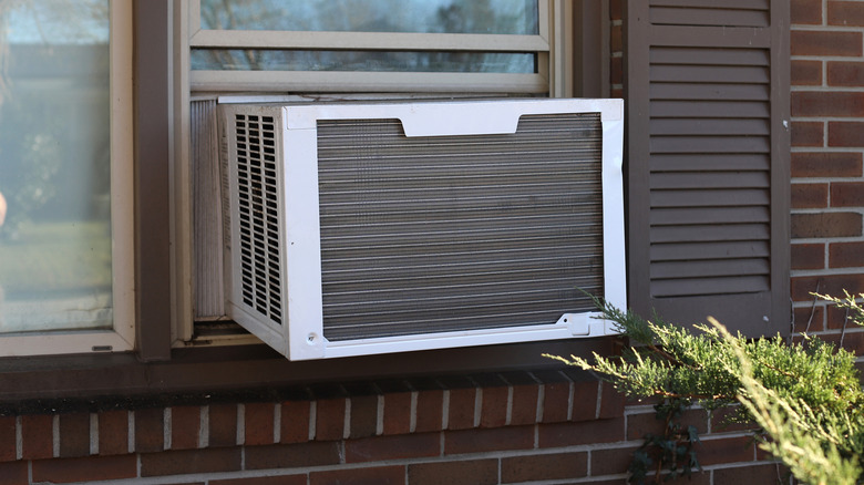 A window air conditioner installed in a brick home with brown shutters