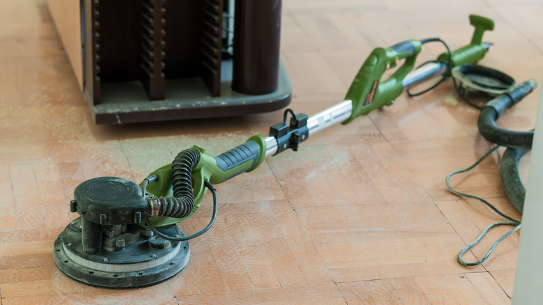 A green power sander sitting on a floor in the process of being refinished