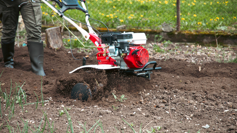 A person in rubber boots using a garden tiller