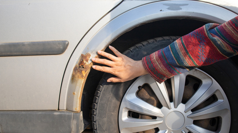 A woman showing rust on the wheel liners of a car