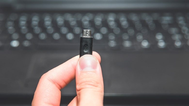 Micro USB connector held in hand with laptop in background