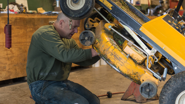 Person working on the underside of a riding mower.