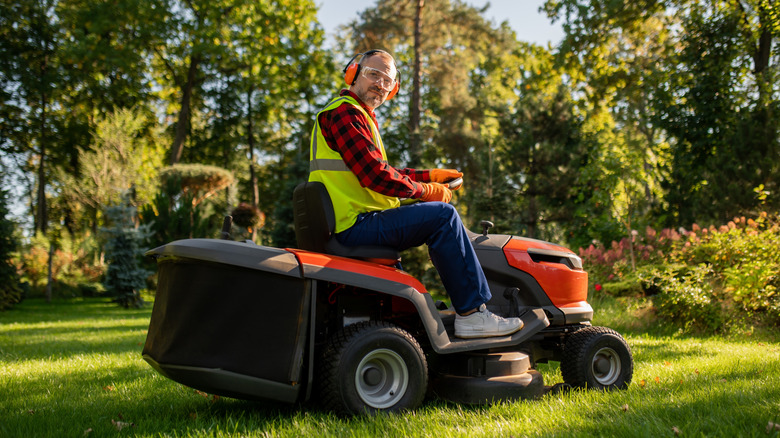 A person driving a riding mower across a stretch of grass.