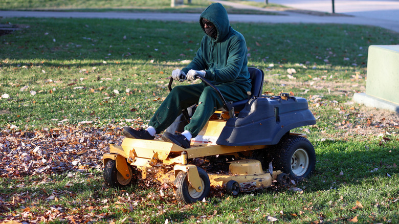 A person rides a riding mower through leaves.