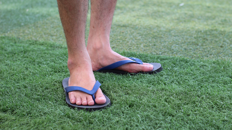 A man wearing blue flip-flops on grass