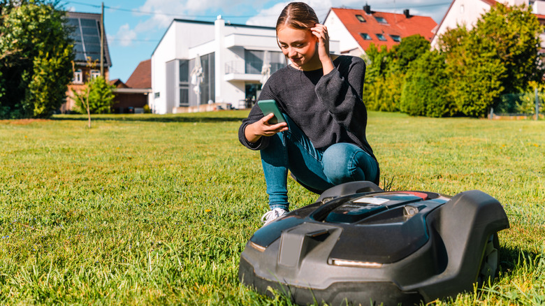 Woman kneeling next to a robot lawn mower.