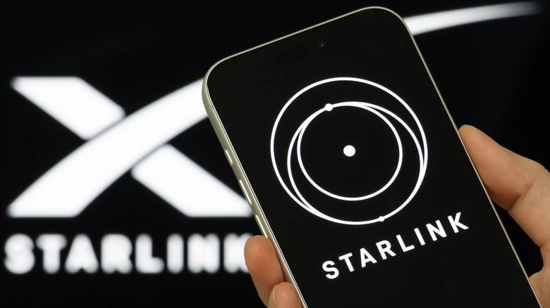 A hand holding a cell phone depicting a white Starlink logo on a black background