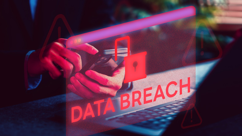 Close-up of a person holding a cell phone near an open laptop with a red data breach icon imposed on top