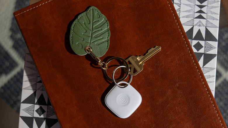 A set of keys with a tile tracker keychain attached sitting on top of a brown leather portfolio