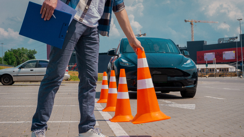 A person placing traffic cones in a row in front of a Tesla during a driving test.