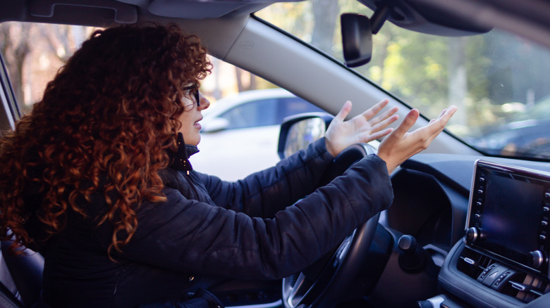 A frustrated female driver raising both hands above the steering wheel.