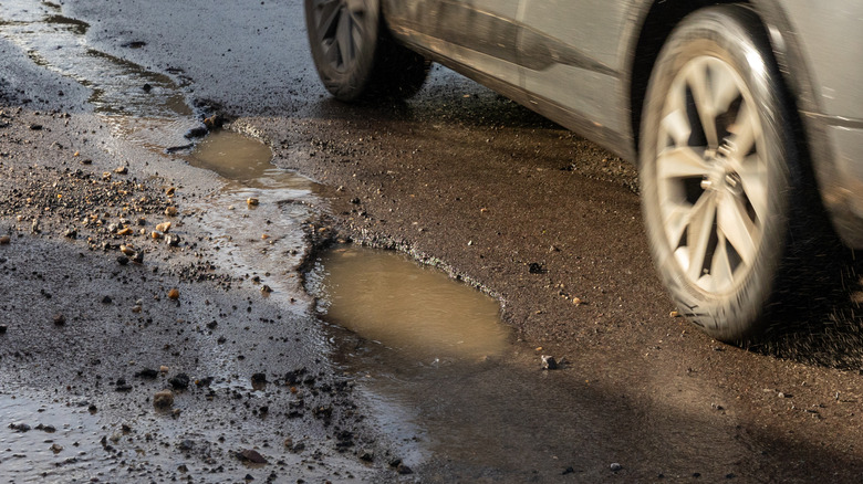 A car passing a pothole in the road.