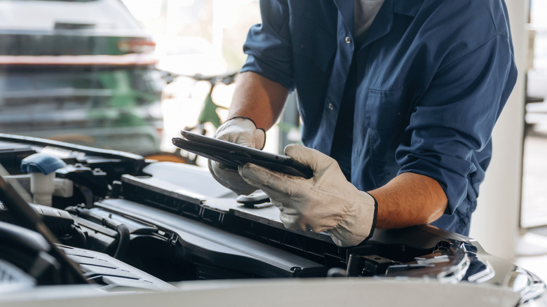 A mechanic looking at his tablet while fixing a car