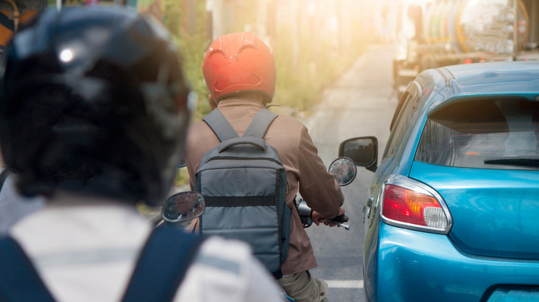 Two bikers riding close behind a car.