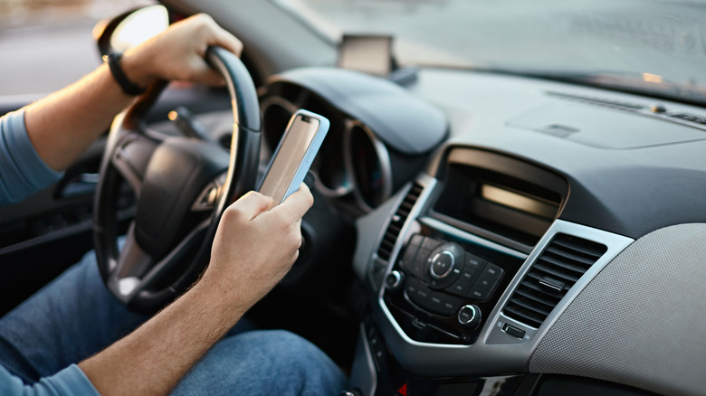 A driver using their mobile phone while driving with one hand